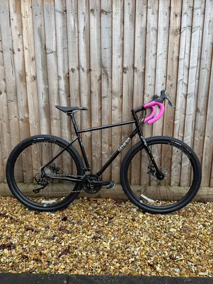 Black gravel bike with pink bar tape and adventure setup